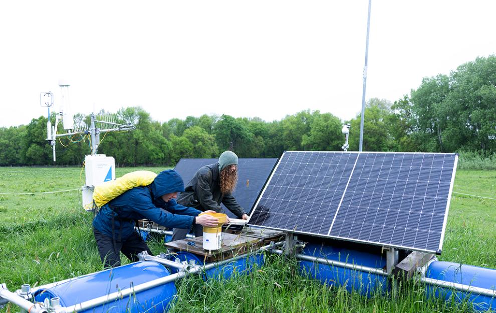 Two researchers working on solar-powered environmental monitoring equipment in a grassy field.